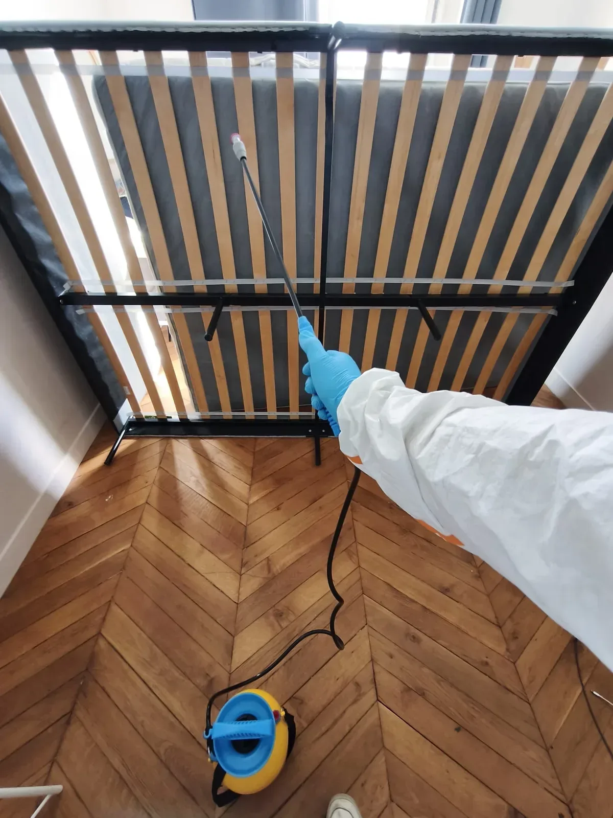Application d'insecticide sur la sous-face d'un sommier au pulvérisateur à pression — traitement punaises de lit Paris 2, quartier Bourse